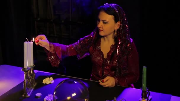Am Tisch im Wahrsagersalon zündet eine Zigeunerin in rotem Kleid Kerzen in einem Kerzenständer an — Stockvideo