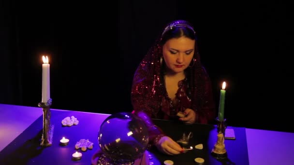 У чарівному салоні циганка запалює свічки на чорному столі — стокове відео