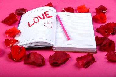 Gül yaprakları tasarımı pembe bir arka plan üzerinde kırmızı keçeli kalem bir not defterinde yazılı kelime aşk.