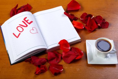 Kırmızı gül yaprakları ile kaplı ahşap bir masa üzerinde bir fincan kahve ve bir günlük kelime ile seviyorum. Yatay fotoğraf.