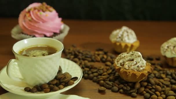 Café em copos brancos, bolos e um espalhamento de grãos de café na mesa . — Vídeo de Stock