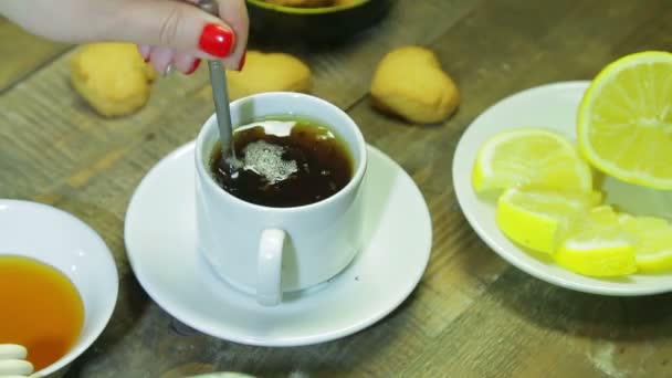 Žena vmíchejte lžíci v bílém cup na dřevěný stůl. Čerstvě uvařeného černého čaje — Stock video