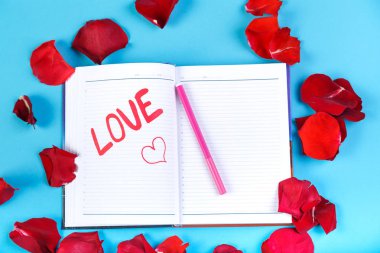 Gül yaprakları tasarım mavi bir arka plan üzerinde kırmızı keçeli kalem bir not defterinde yazılı kelime aşk.