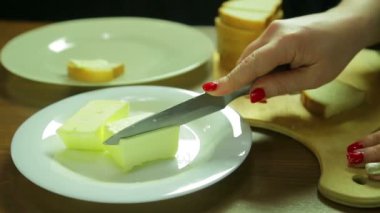Bir kadın bir dilim tereyağı keser ve canap ekmek üzerine tereyağı yayılır.