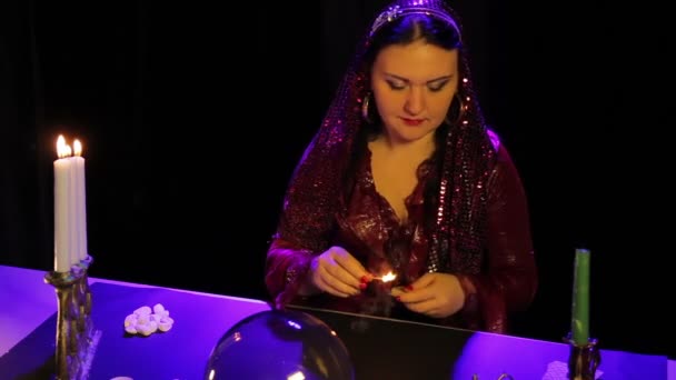 A la table du salon de divination, une gitane dans une robe rouge allume des bougies dans un chandelier sculpté — Video