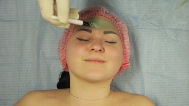 Чоловічий косметолог в рукавичках наносить грязьову маску з пензлем на обличчя жіночого клієнта . — стокове відео
