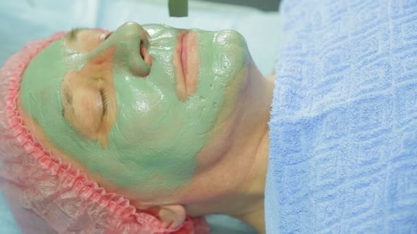 女性美容師は、癒しの泥マスクをブラシで男の顔に適用します。横から見た図 — ストック動画