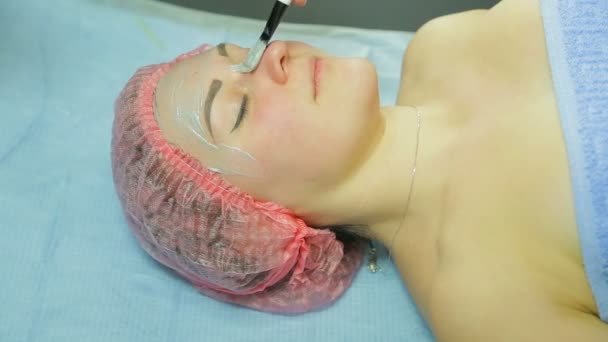 Косметолог в перчатках надевает косметическую маску на лицо женщины. Вид сбоку — стоковое видео