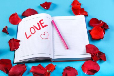 Gül yaprakları tasarım mavi bir arka plan üzerinde kırmızı keçeli kalem bir not defterinde yazılı kelime aşk.