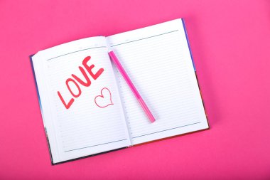 Pembe bir arka plan üzerinde kırmızı keçeli kalem bir not defterinde yazılı kelime aşk.