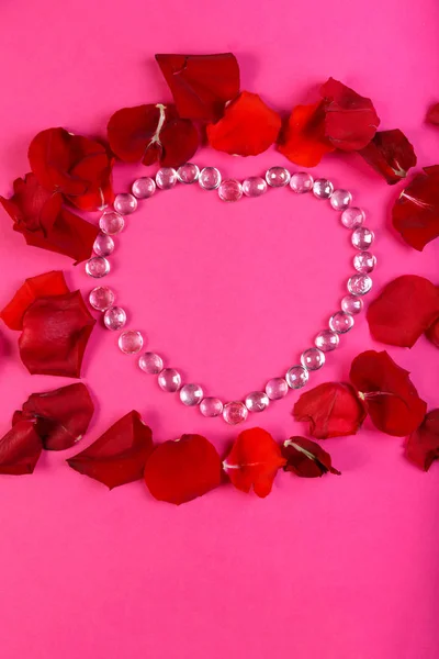 Серце з бісеру на рожевому тлі, прикрашеному пелюстками троянд . — стокове фото