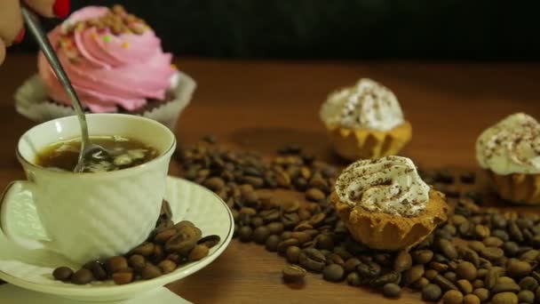 Café em copos brancos. Mulher mexendo com uma colher, bolos e uma dispersão de grãos de café na mesa — Vídeo de Stock