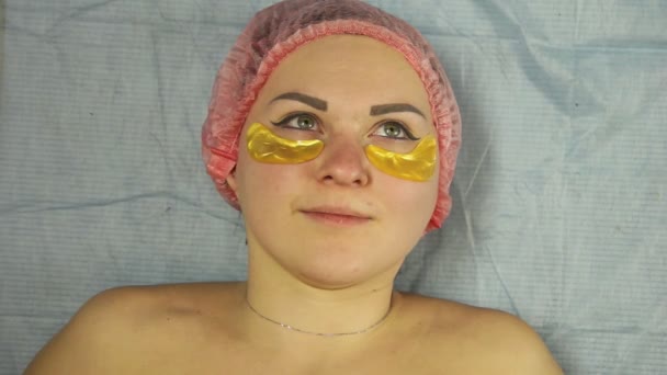 Un cosmétologue masculin dans un gant met des tampons de collagène sur les paupières inférieures d'une femme — Video