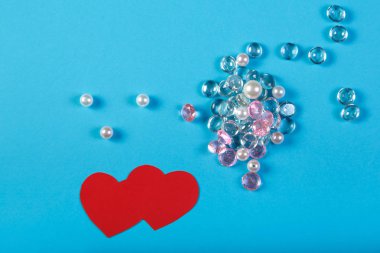 Bir saçılma mavi bir arka plan ve bir kalp kırmızı kağıt beyaz ve pembe taşlar. Dikey fotoğraf