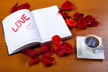 Kırmızı gül yaprakları ile kaplı ahşap bir masa üzerinde bir fincan kahve ve bir günlük kelime ile seviyorum. Yatay fotoğraf.