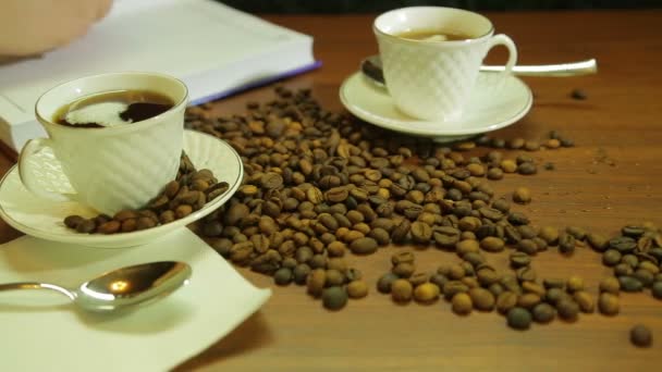 Чашки крепкого кофе, разбрасывание кофейных зерен на столе и женщина ведет дневник — стоковое видео