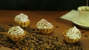 Beyaz fincan kahve. Bir kaşık, kek ve kahve çekirdekleri masada bir saçılma ile karıştırarak bir kadın. Yakın çekim