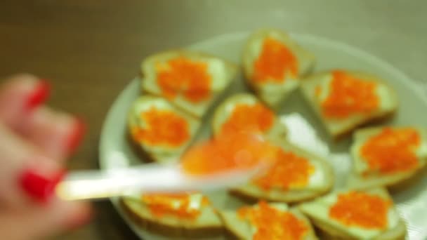 En platta med kanapéer med röd kaviar och en sked med kaviar i en kvinnas hand. — Stockvideo