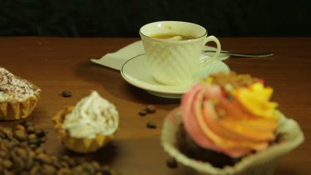 Café em copos brancos, bolos e um espalhamento de grãos de café na mesa — Vídeo de Stock