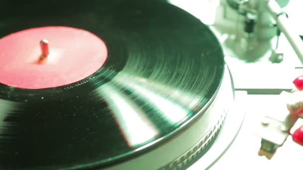 Female hand sets a turntable needle on a vinyl record in color light — Stock Video