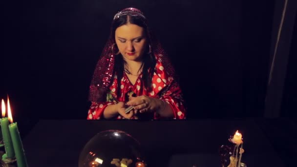 A gypsy fortune teller at the table by candlelight reads the future on the cards in the smoke — Stock Video