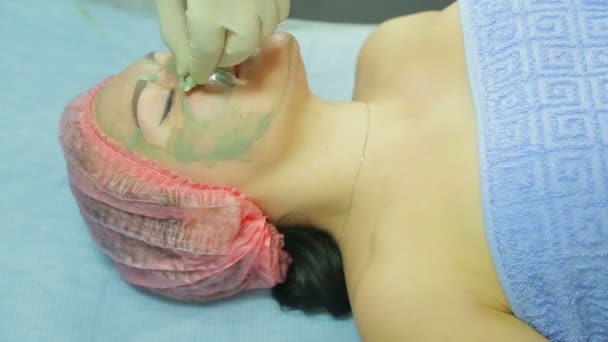Un estetista in guanti rimuove una maschera di argilla dal viso di una donna con un batuffolo di cotone. Vista laterale — Video Stock
