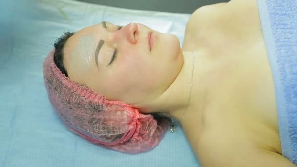 En kvinnlig kosmetolog i handskar gäller en behandlingsmask en mannen s ansikte med en borste. Sidovy. — Stockvideo