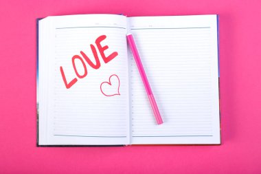 Pembe bir arka plan üzerinde kırmızı keçeli kalem bir not defterinde yazılı kelime aşk.