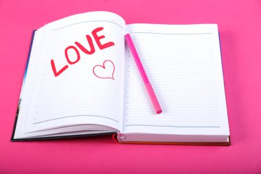 Pembe bir arka plan üzerinde kırmızı keçeli kalem bir not defterinde yazılı kelime aşk. Yatay fotoğraf.