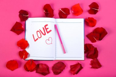 Gül yaprakları tasarımı pembe bir arka plan üzerinde kırmızı keçeli kalem bir not defterinde yazılı kelime aşk.