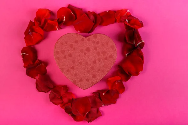 분홍색 배경에 장미 꽃잎으로 둘러싸인 심장의 모양에서 선물 상자. — 스톡 사진