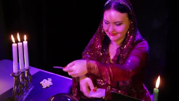Een lachende zigeuner in de magische salon bij kaarslicht leest de toekomst op de kaart — Stockvideo
