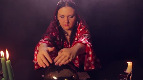 Цыганская гадалка за столом при свечах читает будущее в волшебном кристалле — стоковое видео