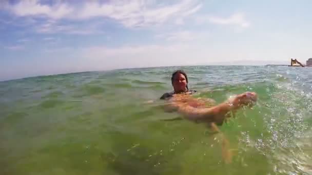 En lycklig kvinna i en svart baddräkt flyter på rygg i havet nära stranden — Stockvideo