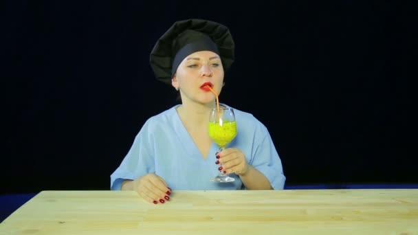 Ένα θηλυκό σεφ σε μαύρο φόντο δοκιμάζει ένα smoothie φρούτων και δείχνει την πινακίδα «τάξη» — Αρχείο Βίντεο
