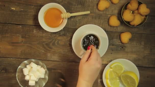 Vrouwelijke hand met thee roeren met een lepeltje in een witte kop op een houten tafel — Stockvideo