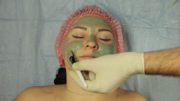 Мужчина-косметолог в перчатках надевает маску на лицо клиента специальной щеткой — стоковое видео