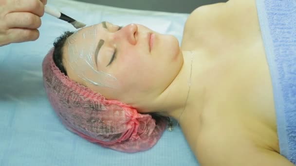 Un'estetista in guanti mette una maschera cosmetica sul viso di una donna. Vista laterale — Video Stock