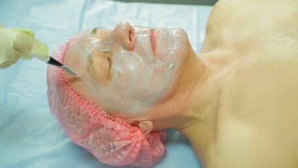 Una cosmetologa donna che indossa guanti applica una maschera di alghe al viso di un uomo con un pennello — Video Stock