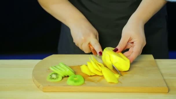 Frauenhände Schneiden Kiwi Und Mangostücke Auf Einem Holzbrett Der Durchschnittliche — Stockvideo