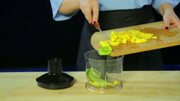 Womens handen leg gesneden kiwi en mango in een blender kom — Stockvideo