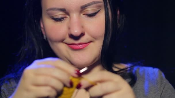 Eine junge lächelnde brünette Frau auf schwarzem Hintergrund strickt auf runden Nadeln aus gelbem Faden — Stockvideo