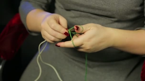 Womans hands on a black background dials on the spokes of a loop of green thread — Stock Video