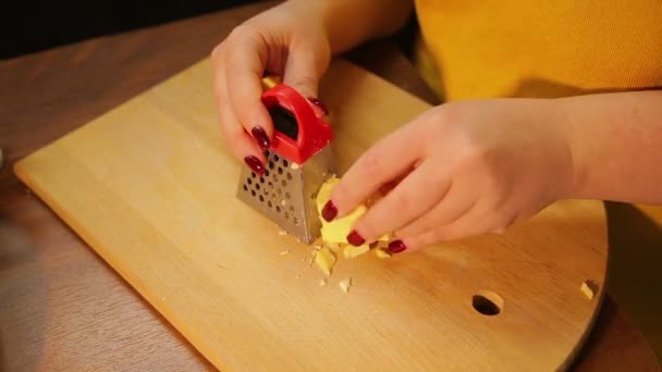 A woman is rubbing cheese for a salad on a coarse grater — Stock Video