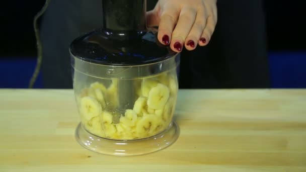 Жінка нарізає банан у мисці для блендерів — стокове відео