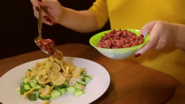 Eine Frau mit einem Löffel legt rote Bohnen in einen Teller mit Salat — Stockvideo