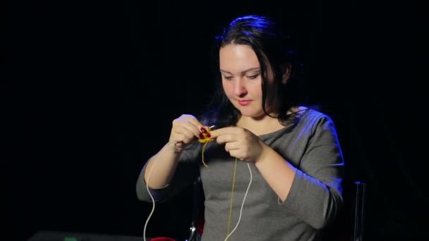 黒い背景に若いブルネットの女性は黄色い糸から針が円形編みのニットします。 — ストック動画