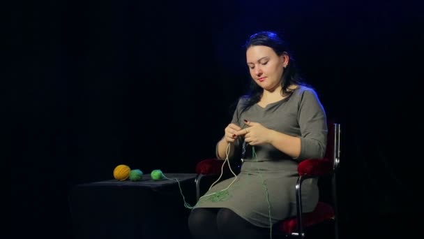 Eine junge brünette Frau auf schwarzem Hintergrund schlingt auf den Stricknadeln mit grünen Fäden — Stockvideo