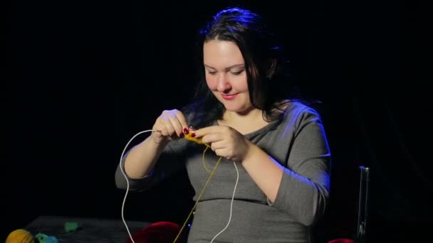 Uma jovem morena em um fundo preto tricota em agulhas circulares — Vídeo de Stock