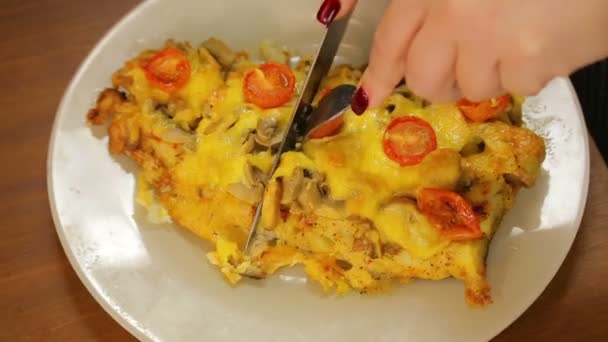 Uma mulher com uma faca e garfo corta queijo de peixe assado com cogumelos e tomates cereja em um prato branco — Vídeo de Stock